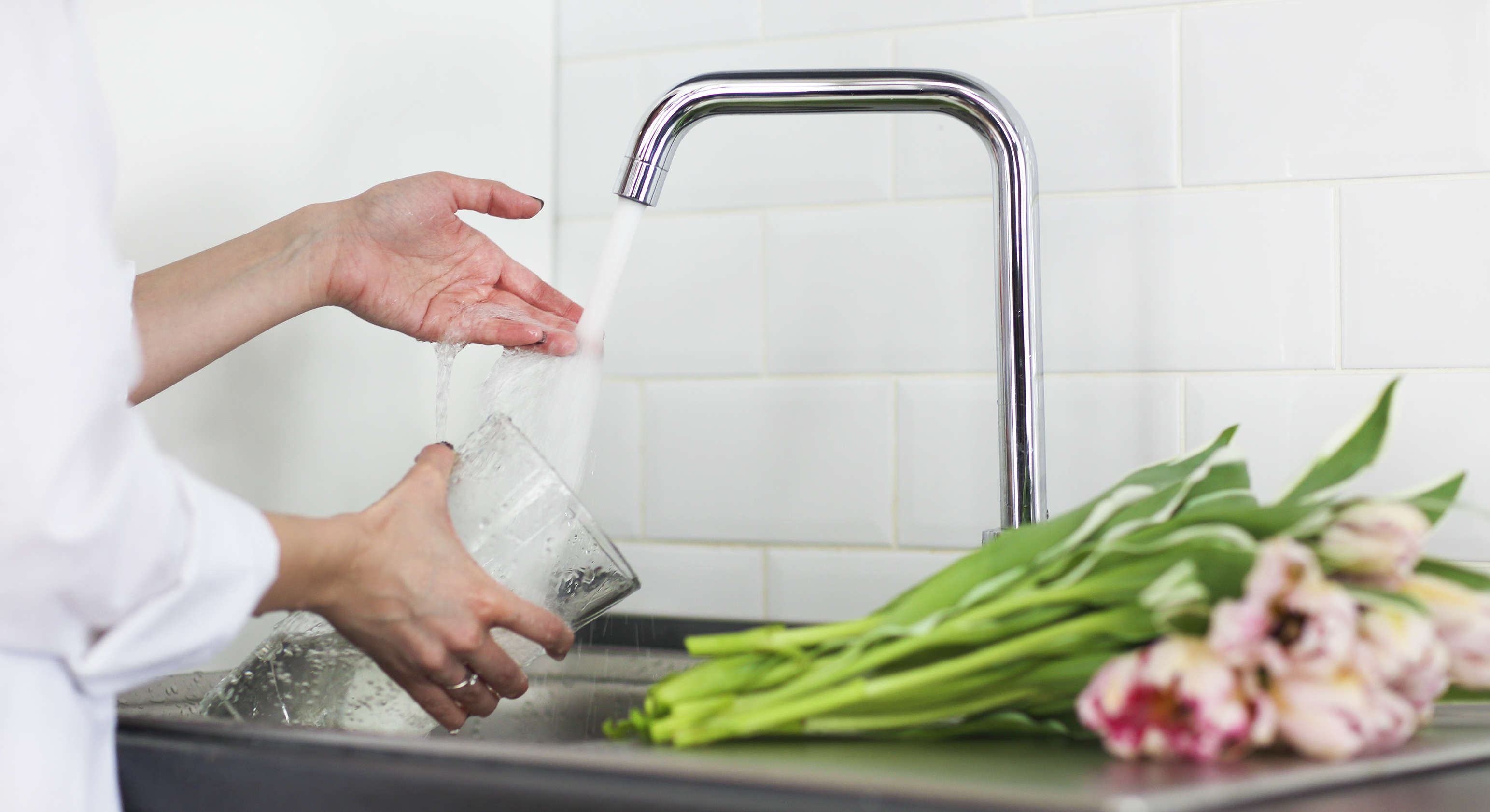 A woman pours sweet water into a glass vase with tulips on the side