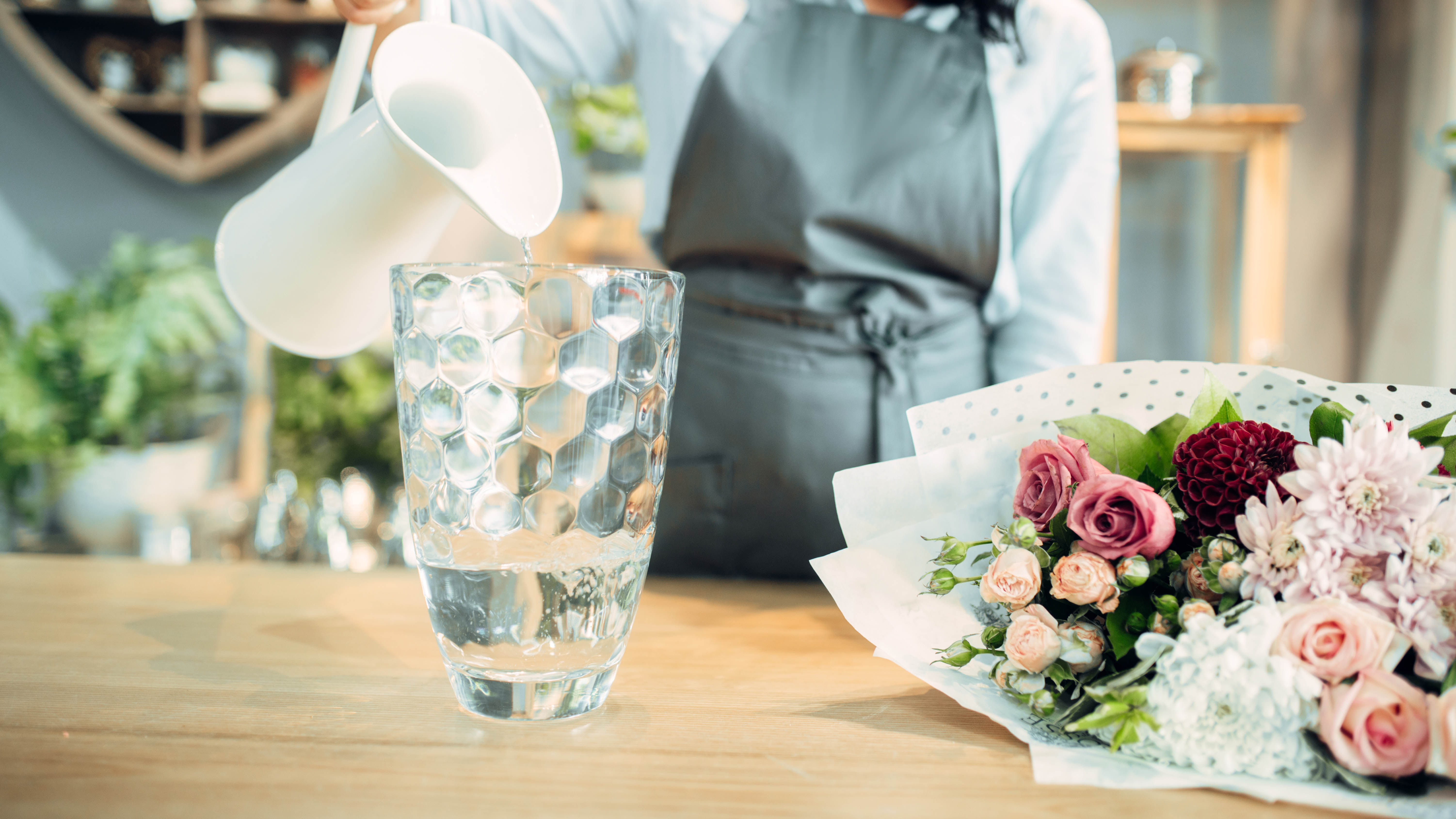 A pitcher pours water into a vase next to a bouquet of flowers