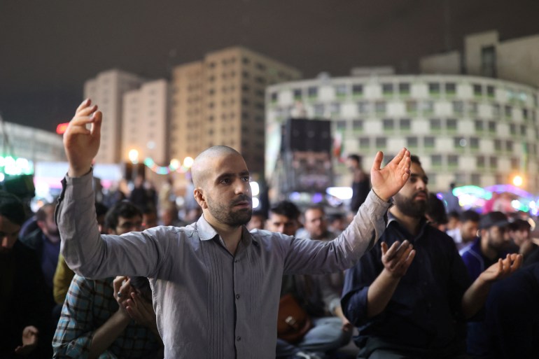 People praying for the well-being of Iran's President Ebrahim Raisi. A man at the front of the crowd has his arms outstretched.